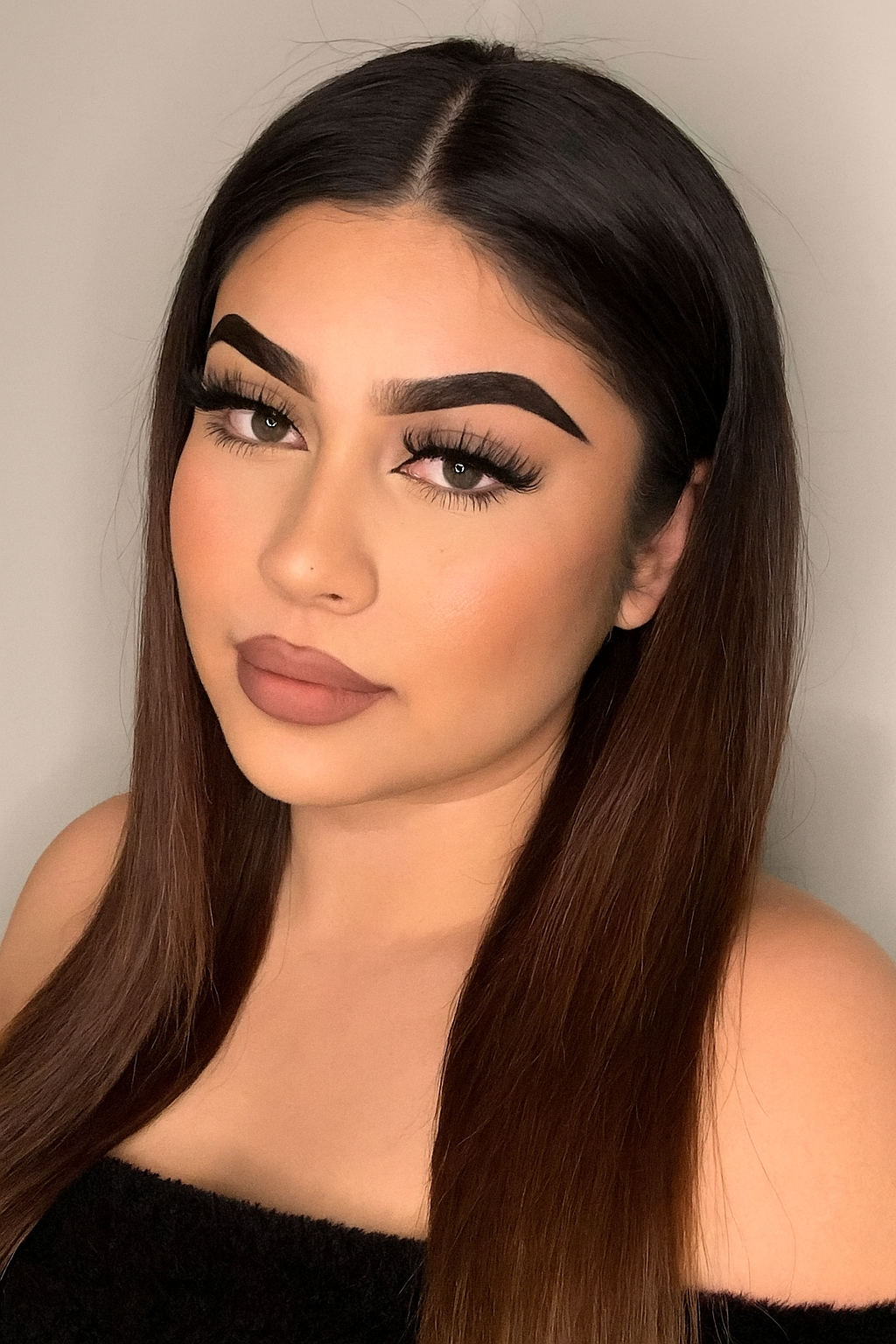 Woman with long brown hair and makeup against a neutral background