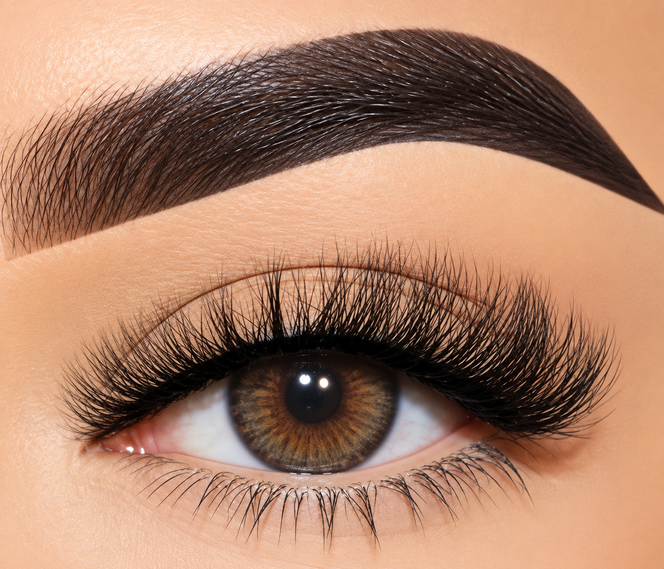 Extreme close-up of a human eye with long, curled black false eyelashes and a dark, well-defined eyebrow on warm beige skin.