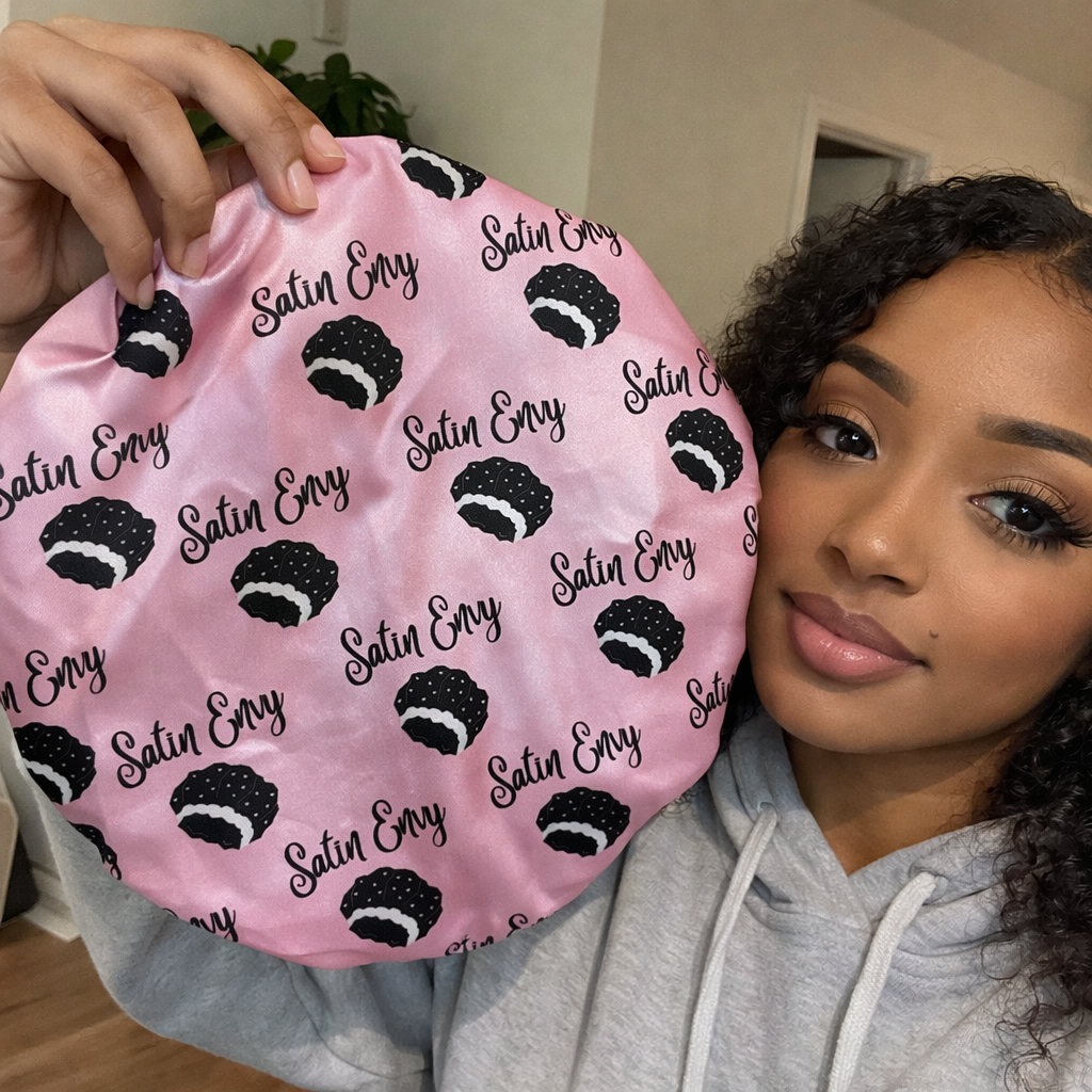 Person holding a pink satin Envy hair bonnet with black logos.