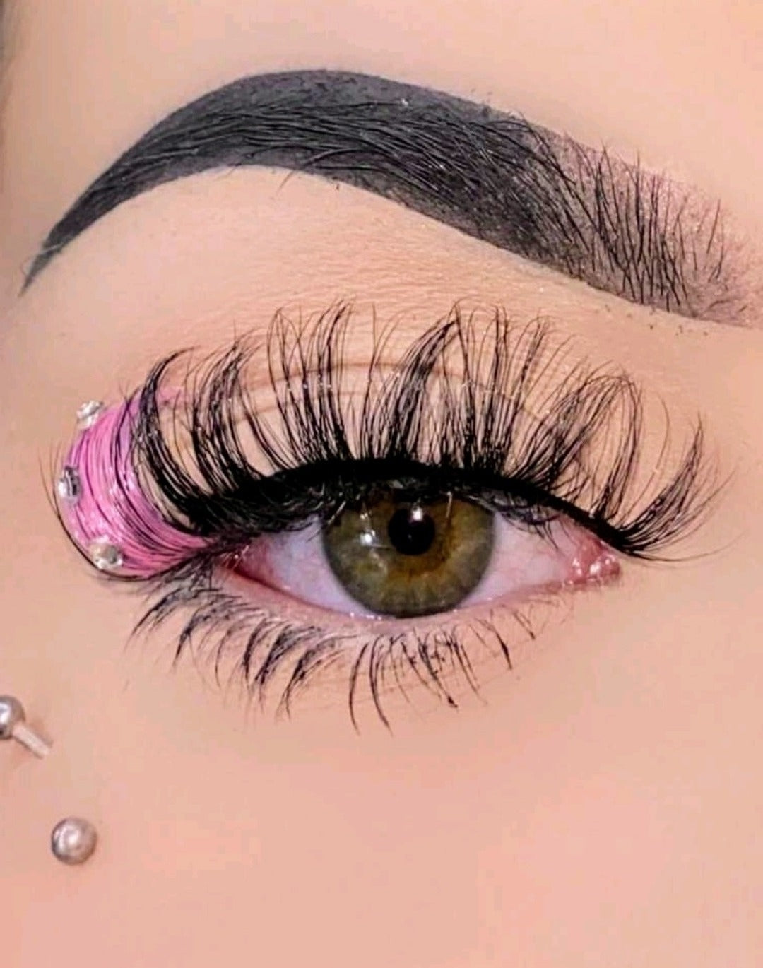 A close-up image of a person wearing pink diamond-shaped false eyelashes with bejeweled accents.