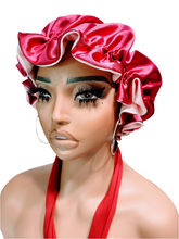 A mannequin head wearing a reversible pink and red satin hair bonnet with a bow.