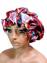 A mannequin head wearing a multicolored reversible satin hair bonnet with a red and blue pattern on one side and a plain white satin bonnet on the other.