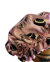 Pink satin bonnet with black text and patterns on a white background