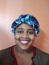 Person wearing a blue satin bonnet against a pink background