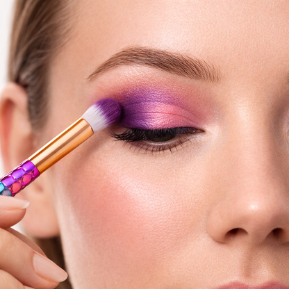 Close-up of a person applying purple makeup to their eyelid with a brush.