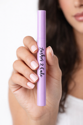 Hand holding a purple makeup product with &